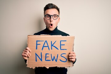 Young handsome caucasian man holding protest carboard for desinformation and fake news scared in shock with a surprise face, afraid and excited with fear expression