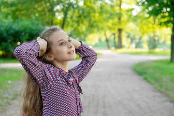 A posing girl 11 years old on a road in a park. Against a background of trees and grass.