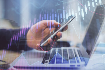 Double exposure of man's hands holding and using a phone and financial graph drawing. Analysis concept.