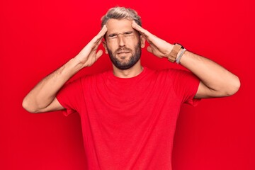 Young handsome blond man wearing casual red t-shirt standing over isolated red background with hand on head, headache because stress. Suffering migraine.
