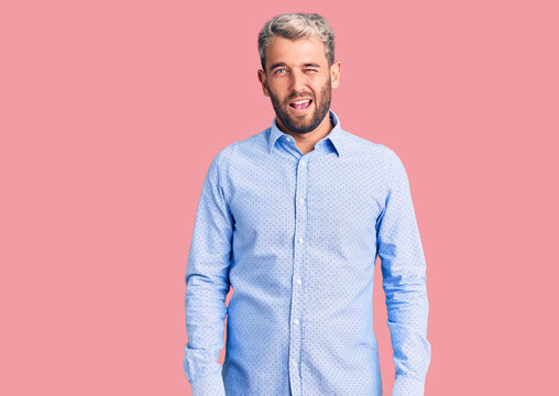 Young handsome blond man wearing elegant shirt winking looking at the camera with sexy expression, cheerful and happy face.