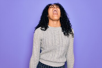 Young african american woman wearing casual sweater and glasses over purple background angry and mad screaming frustrated and furious, shouting with anger. Rage and aggressive concept.