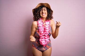 Young beautiful arab woman on vacation wearing swimsuit and hawaiian lei flowers very happy and excited doing winner gesture with arms raised, smiling and screaming for success. Celebration concept.