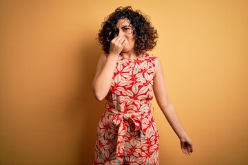 Young beautiful curly arab woman on vacation wearing summer floral dress and sunglasses smelling...