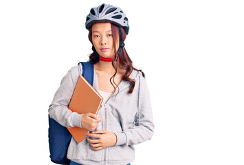 Young beautiful chinese girl wearing student backpack and bike helmet holding book thinking attitude and sober expression looking self confident