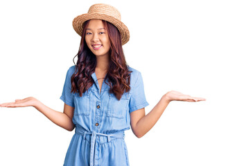 Obraz na płótnie Canvas Young beautiful chinese girl wearing summer hat smiling showing both hands open palms, presenting and advertising comparison and balance