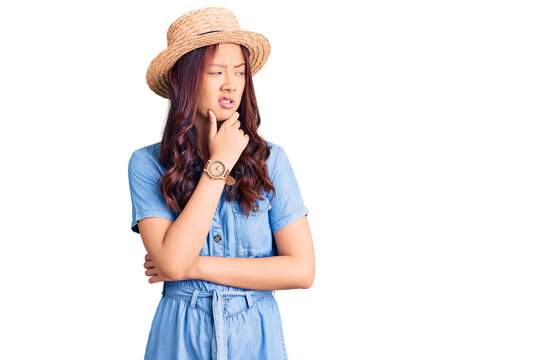 Young beautiful chinese girl wearing summer hat thinking worried about a question, concerned and nervous with hand on chin