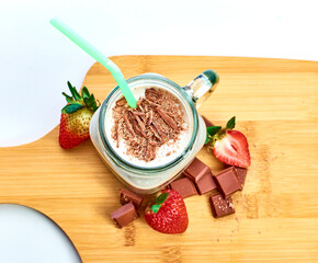 Chocolate milkshake with strawberries and pieces of chocolate on wooden table and white background