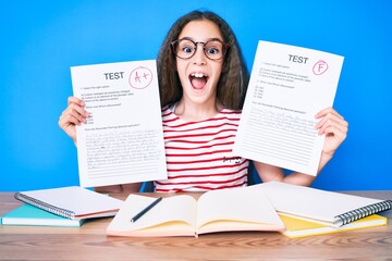 Cute hispanic girl showing failed and passe exam sitting on the table celebrating crazy and amazed for success with open eyes screaming excited.