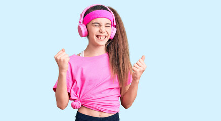 Obraz na płótnie Canvas Cute hispanic child girl wearing gym clothes and using headphones very happy and excited doing winner gesture with arms raised, smiling and screaming for success. celebration concept.