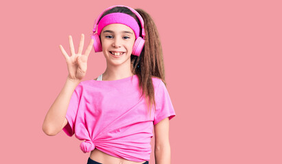 Obraz na płótnie Canvas Cute hispanic child girl wearing gym clothes and using headphones showing and pointing up with fingers number four while smiling confident and happy.