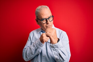 Middle age handsome hoary man wearing casual striped shirt and glasses over red background Ready to fight with fist defense gesture, angry and upset face, afraid of problem