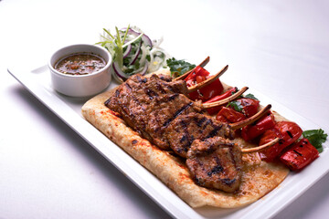 Pork, lamb ribs on pita bread, with baked bell pepper and sauce, on a white plate