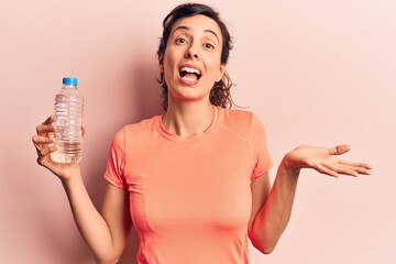 Young beautiful hispanic woman drinking bottle of water celebrating achievement with happy smile and winner expression with raised hand