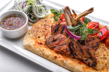 Pork, lamb ribs on pita bread, with baked bell pepper and sauce, on a white plate