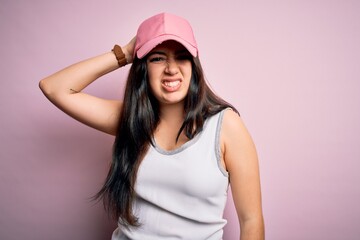 Young brunette woman wearing casual sport cap over pink background confuse and wonder about question. Uncertain with doubt, thinking with hand on head. Pensive concept.