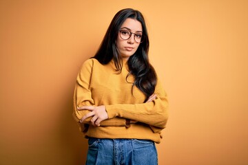 Young brunette woman wearing glasses and casual sweater over yellow isolated background looking...