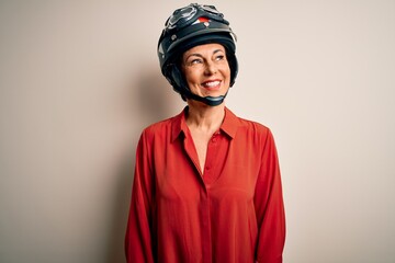 Middle age motorcyclist woman wearing motorcycle helmet over isolated white background looking away to side with smile on face, natural expression. Laughing confident.