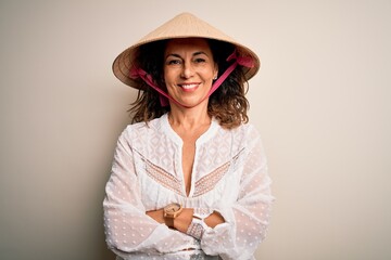 Middle age brunette woman wearing asian traditional conical hat over white background happy face smiling with crossed arms looking at the camera. Positive person.