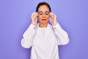 Middle age senior scientist woman wearing coat and laboratory glasses over purple background suffering from headache desperate and stressed because pain and migraine. Hands on head.