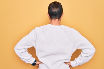 Young handsome man with blue eyes wearing casual sweater standing over yellow background standing...