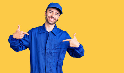 Young hispanic man wearing painter uniform looking confident with smile on face, pointing oneself...