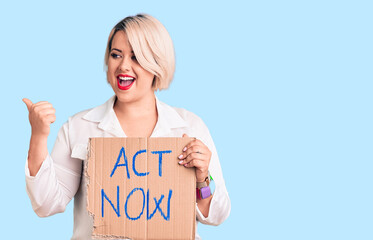 Young blonde plus size woman holding act now cardboard banner pointing thumb up to the side smiling happy with open mouth