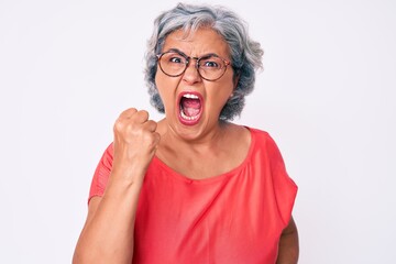 Senior hispanic grey- haired woman wearing casual clothes and glasses angry and mad raising fist frustrated and furious while shouting with anger. rage and aggressive concept.
