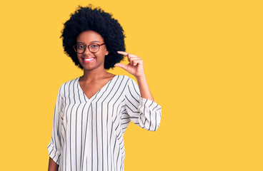Young african american woman wearing casual clothes and glasses smiling and confident gesturing with hand doing small size sign with fingers looking and the camera. measure concept.