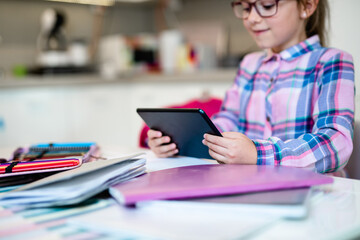 Cute little girl holding tablet while doing her homework. Online education.