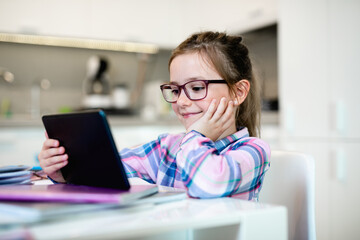 Cute little girl holding tablet while doing her homework. Online education.