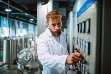 Switchboard operator controlling machine in production plant. Caucasian technologist specialist in white protective suit working in food and beverage factory.