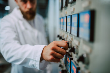 Switchboard operator controlling machine in production plant. Caucasian technologist specialist in white protective suit working in food and beverage factory.