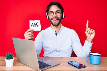 Handsome hispanic man working at the office holding 4k  banner smiling happy pointing with hand and finger to the side