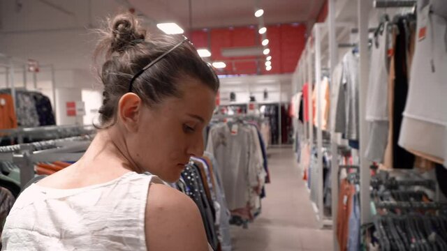 Smiling young girl choosing new clothes ini shopping mall