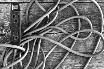 A black and white image of an old tangle electrical cord on a wooden work table. 