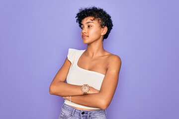 Young beautiful african american afro woman wearing casual t-shirt over purple background looking to the side with arms crossed convinced and confident