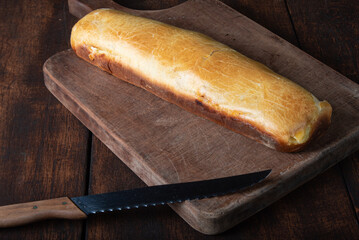 Homemade bread stuffed with shredded chicken on rustic wood and knife with black background, selective focus.
