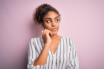 Young beautiful african american girl wearing striped t-shirt standing over pink background with hand on chin thinking about question, pensive expression. Smiling with thoughtful face. Doubt concept.