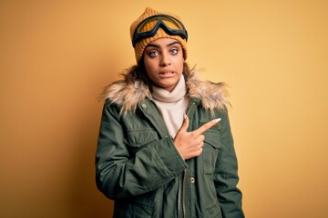 Young african american afro skier girl wearing snow sportswear and ski goggles Pointing aside worried and nervous with forefinger, concerned and surprised expression