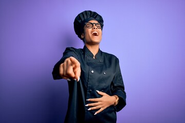 Young african american chef girl wearing cooker uniform and hat over purple background laughing at you, pointing finger to the camera with hand over body, shame expression