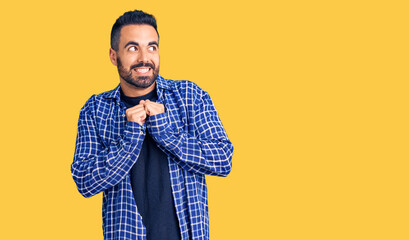 Young hispanic man wearing casual clothes laughing nervous and excited with hands on chin looking to the side