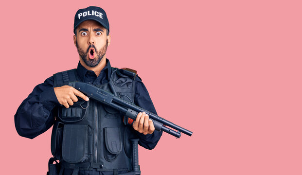 Young hispanic man wearing police uniform holding shotgun scared and amazed with open mouth for surprise, disbelief face