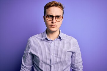Obraz premium Young handsome redhead man wearing casual shirt and glasses over purple background skeptic and nervous, frowning upset because of problem. Negative person.