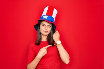 Young beautiful brunette woman wearing united states hat celebrating independence day In hurry pointing to watch time, impatience, looking at the camera with relaxed expression