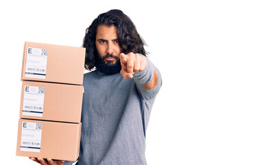 Young arab man holding delivery package pointing with finger to the camera and to you, confident gesture looking serious