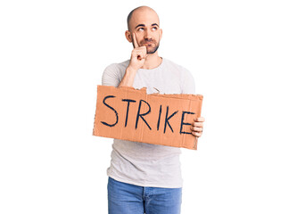 Young handsome man holding strike banner serious face thinking about question with hand on chin, thoughtful about confusing idea