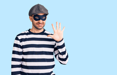 Fototapeta premium Young handsome man wearing burglar mask showing and pointing up with fingers number five while smiling confident and happy.