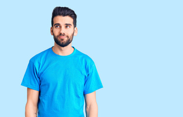 Young handsome man with beard wearing casual t-shirt smiling looking to the side and staring away thinking.
