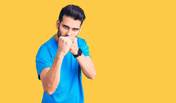 Young handsome man with beard wearing casual t-shirt ready to fight with fist defense gesture, angry and upset face, afraid of problem